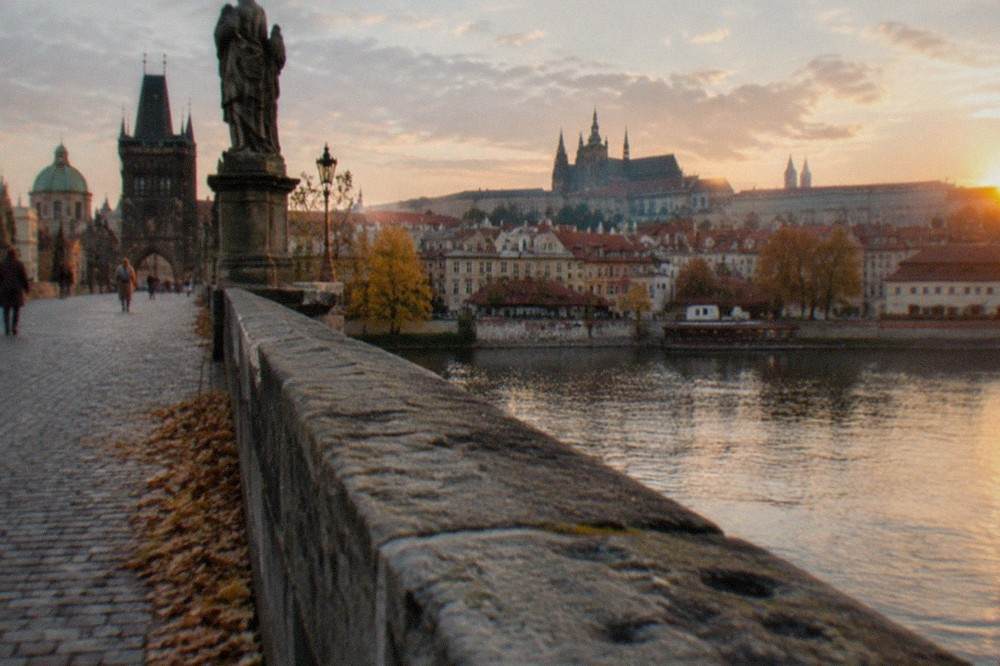 Vista sin multitudes del Puente de Carlos y el río Moldava con las torres del Castillo de Praga al fondo a la hora dorada