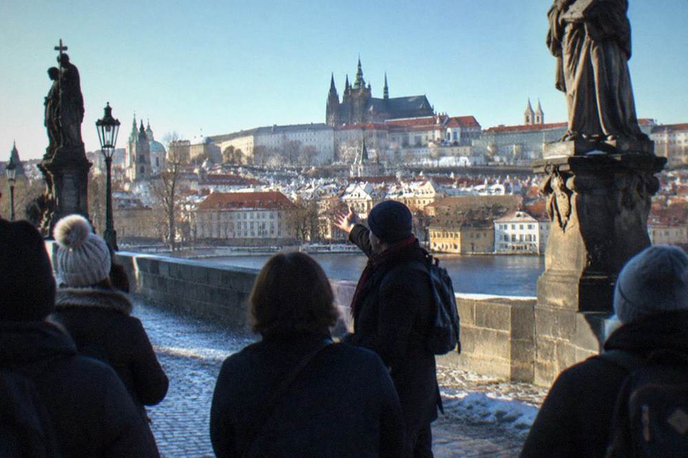 Un guía local señalando hacia las torres del Castillo de Praga mientras un grupo de turistas está en el Puente de Carlos