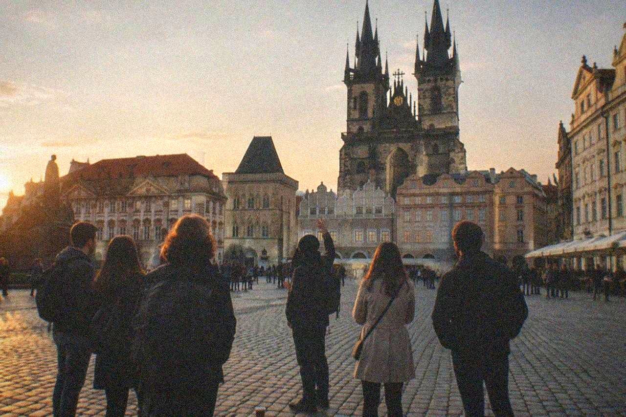 A walking tour guide speaking to a small group gathered on a cobbled square in Prague at golden hour