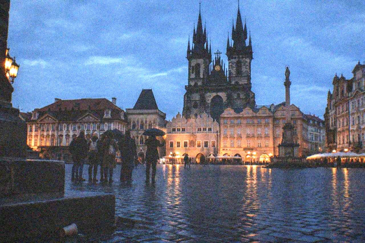 A guide holding a small group gathered on a cobbled square in Prague at dusk