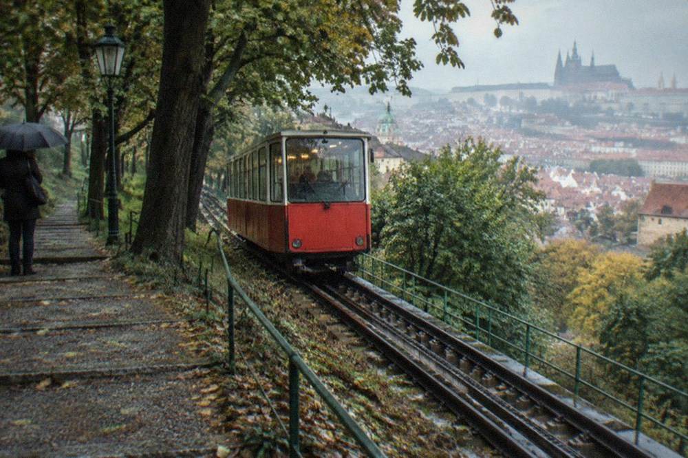 Funicular railway car on an inclined track climbing through trees beside a stepped path
