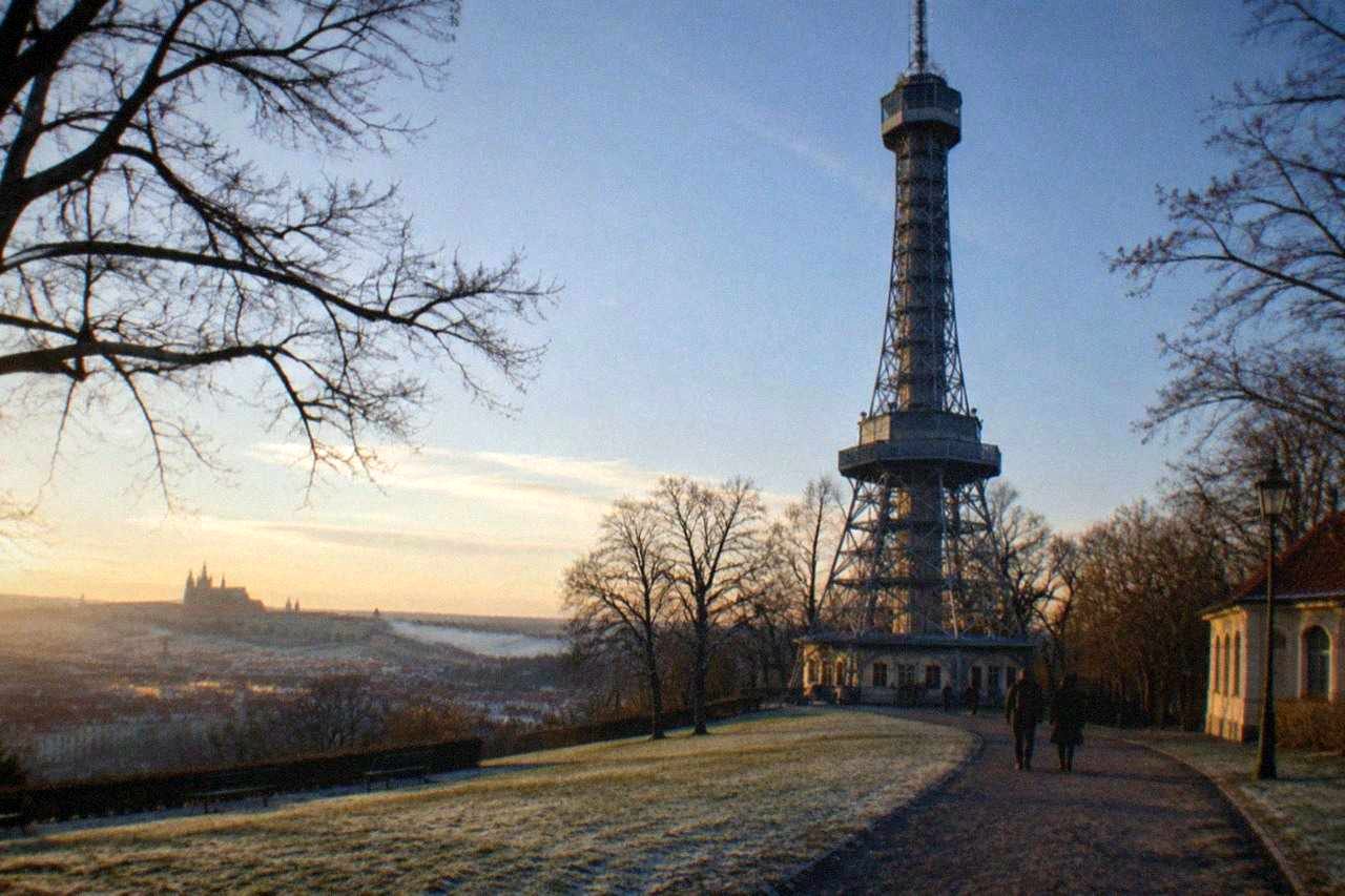 Steel lookout tower rising above wooded parkland on a hill above city rooftops