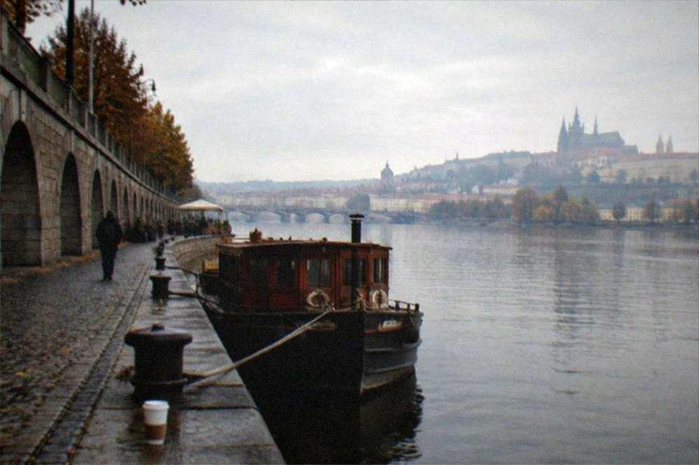 Riverside promenade along the Vltava with bridge arches and a castle silhouette in the distance