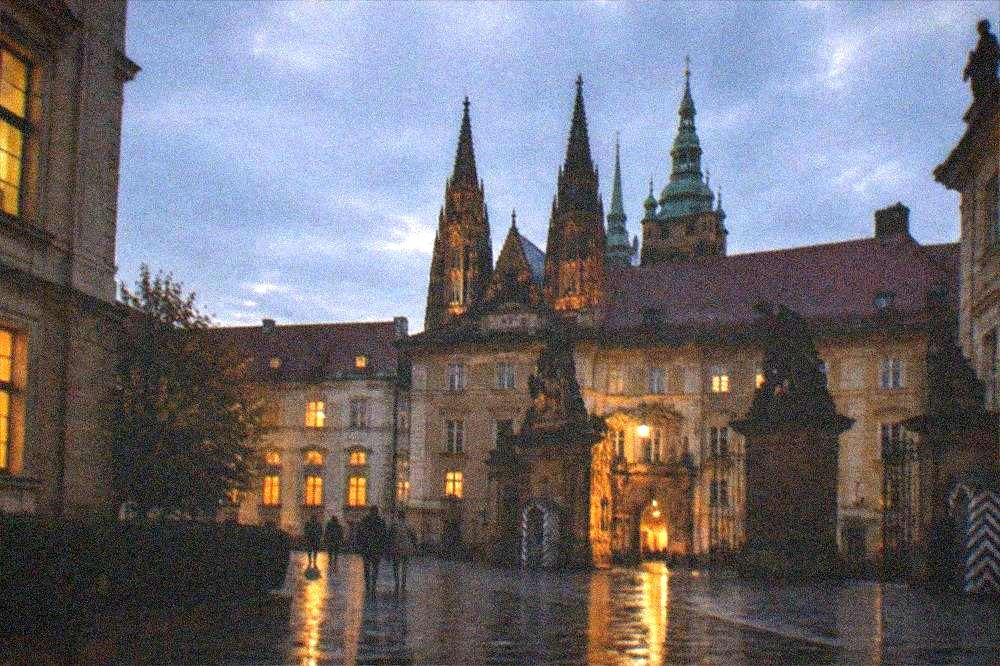 Patio del Castillo de Praga bajo un cielo vespertino con ventanas iluminadas en los edificios antiguos