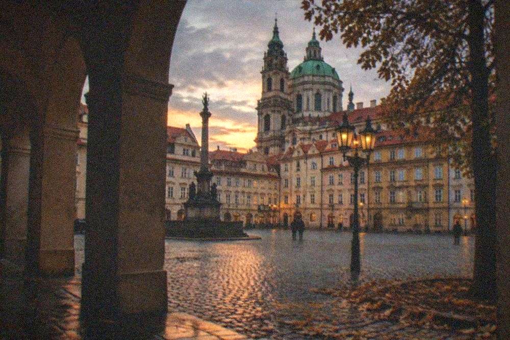 A cobbled Prague square with historic facades and a church tower at dusk