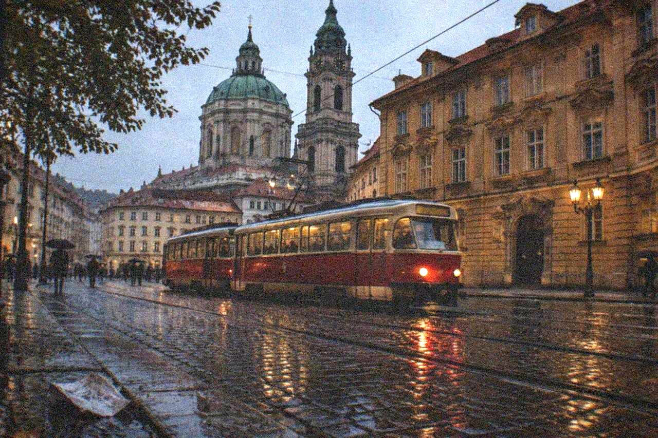 A red Prague tram moving along a street with historic buildings on both sides