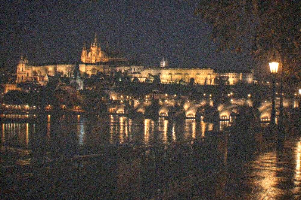 Vista nocturna al otro lado del río Moldava hacia el Castillo de Praga y el perfil del Puente de Carlos
