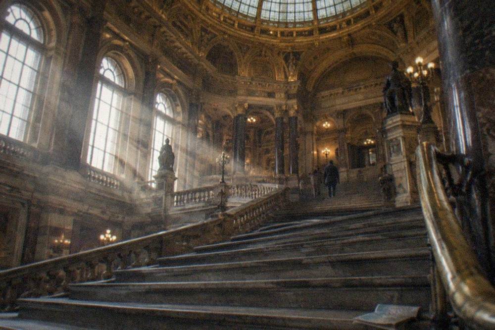 Gran salón de museo con escalera de mármol y ventanas altas de arco iluminadas por luz natural