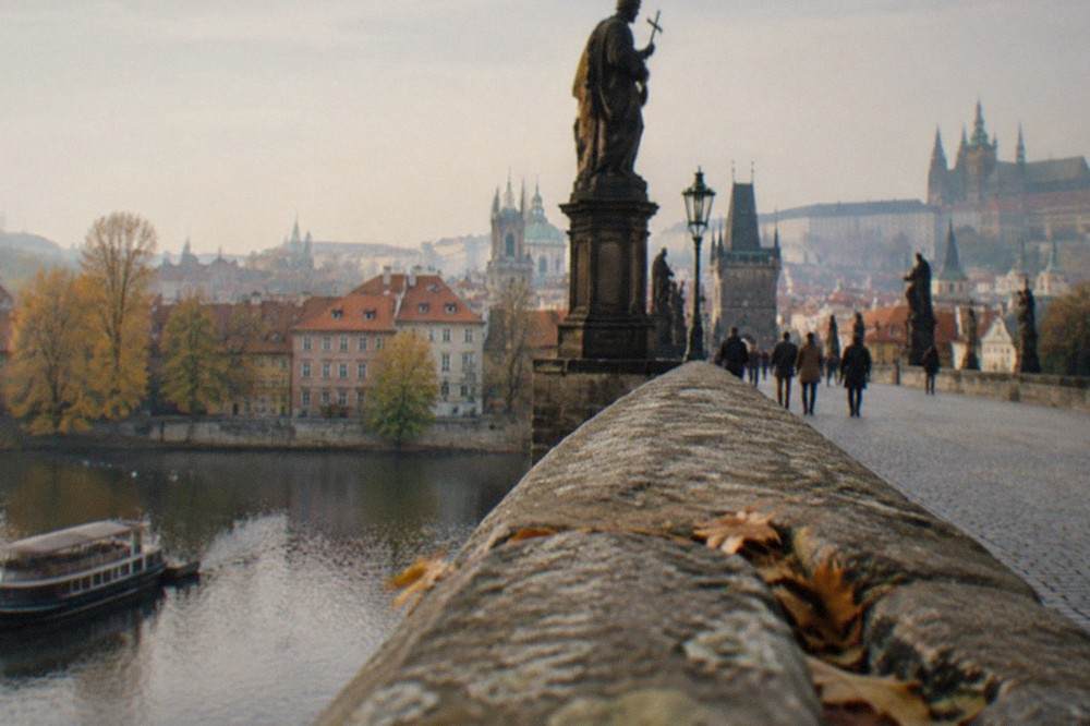 Pedestrians crossing Charles Bridge with statue silhouettes and the river below
