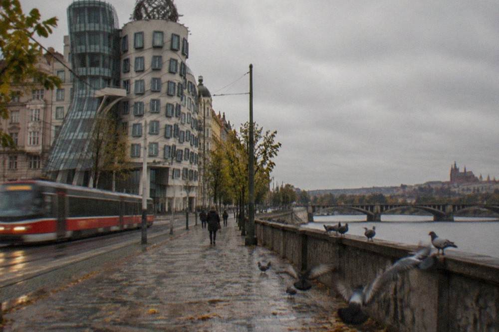 The Dancing House seen from the Vltava riverside promenade with tram tracks along the embankment