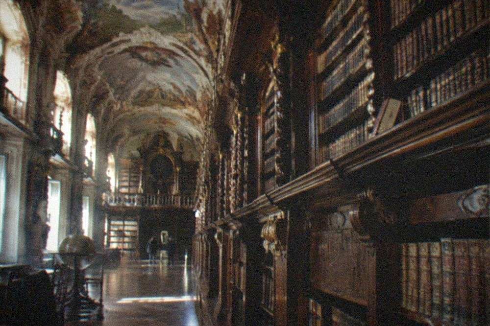 Ornate baroque library hall with tall wooden bookshelves and a painted ceiling