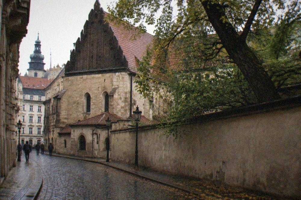 Old synagogue exterior with a red roof and historic cemetery trees behind a wall