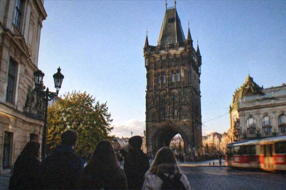 Guided group of visitors listening to a guide beside historic buildings on a Prague street