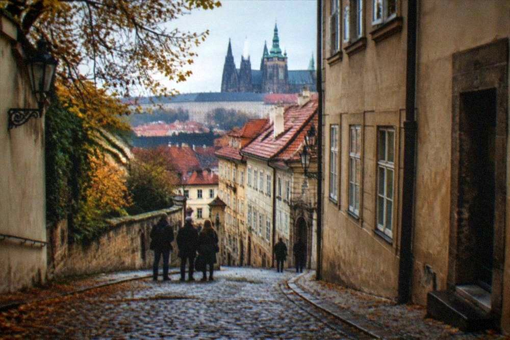 A walking tour group pausing on the cobbled lane below Prague Castle with the cathedral spires above