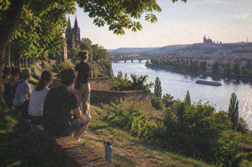 A guide addressing a seated group of visitors on the ramparts above the Vltava river at Vysehrad