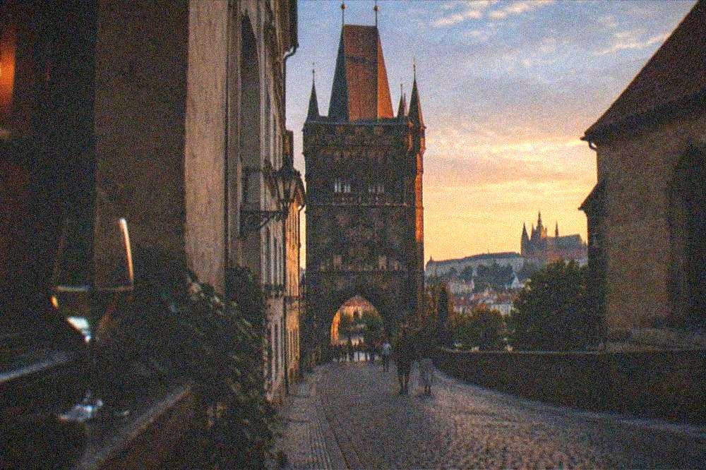 Historic Prague street with a view toward a bridge tower at dusk