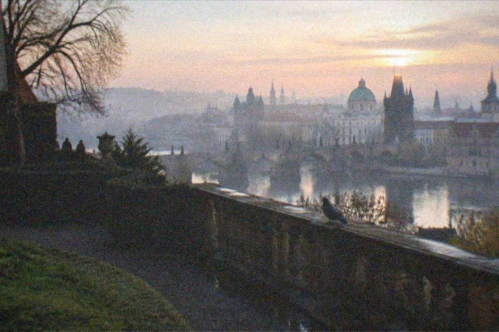 A stone bridge and domes seen from a high green hillside above a river