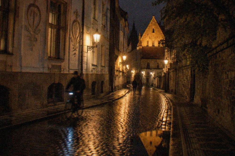 A narrow old street lit by warm lanterns against a dark evening sky