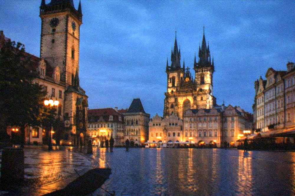 A gothic church facade and old town hall tower lit up above a dark square