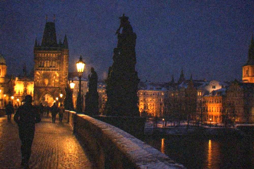 A historic stone bridge with statues and lit towers spanning a dark river