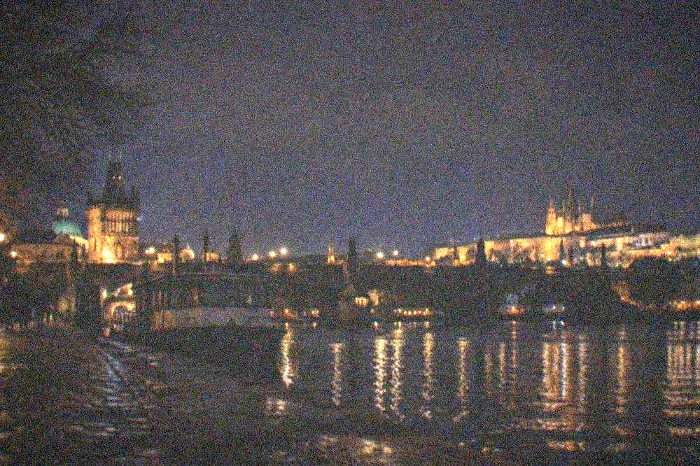 Charles Bridge and the lit towers of Prague at night seen from the Vltava riverbank