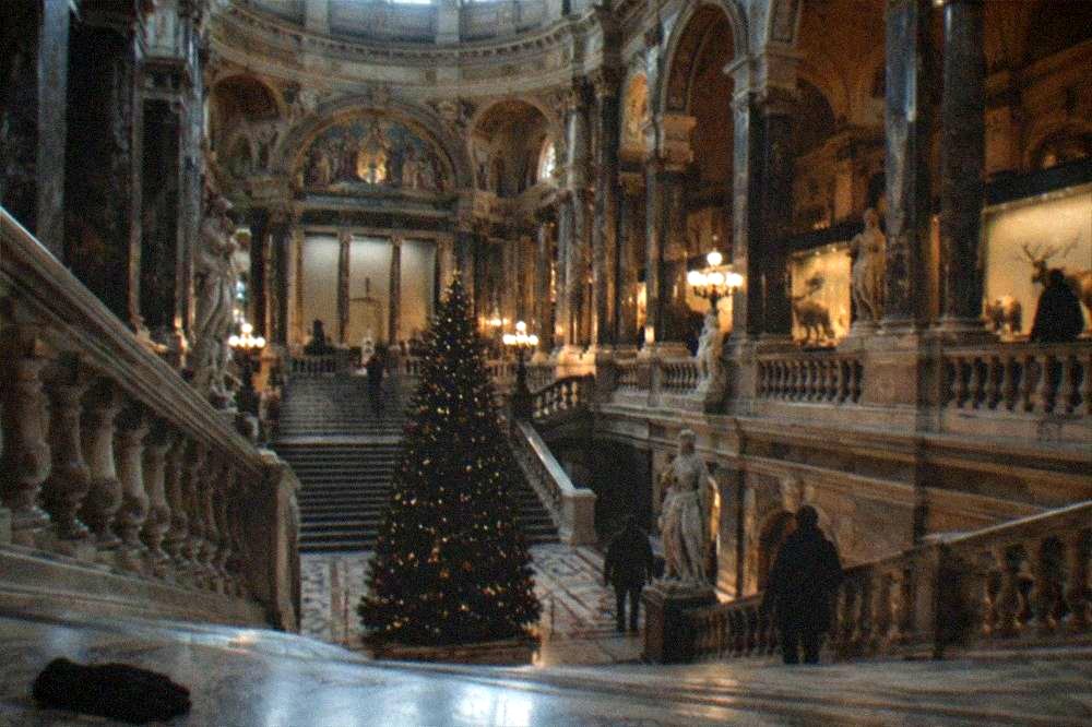 A grand museum hall with a Christmas tree and visitors browsing exhibits
