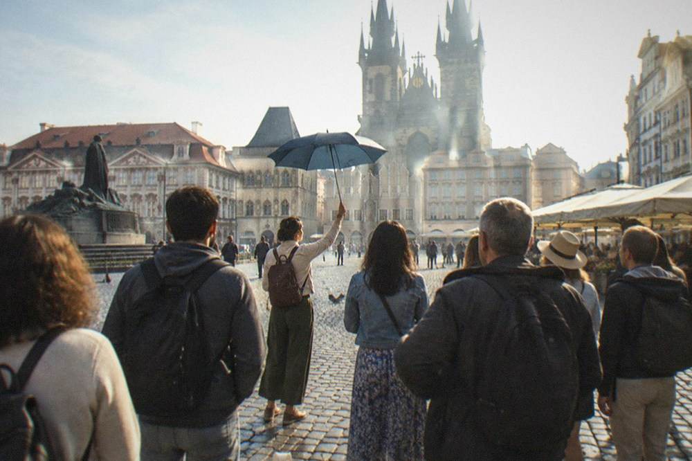 A crowd gathered in Old Town Square around a guide holding up a sign