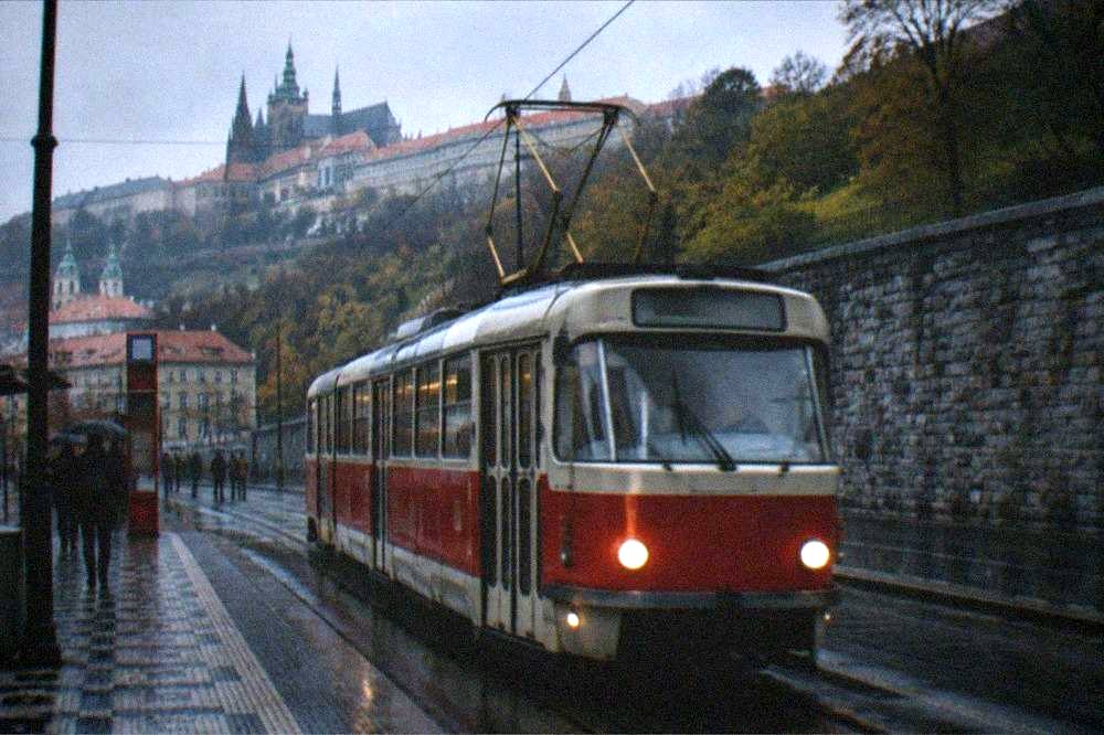 A red Prague tram passing along a street lined with historic apartment buildings