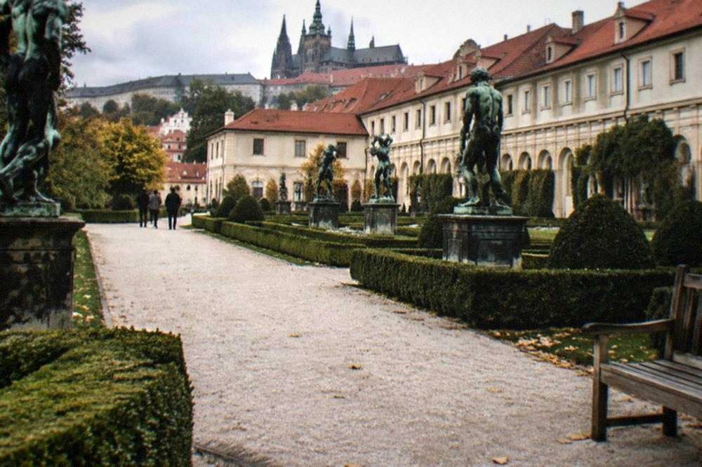 Jardín barroco formal con estatuas y senderos de grava junto a una pared de palacio