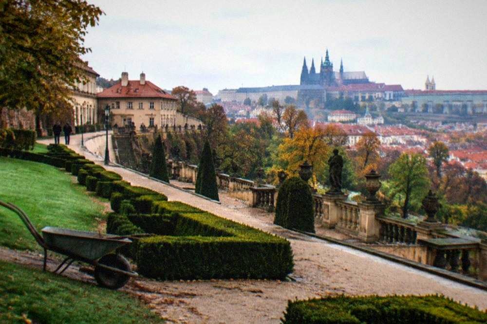 Formal renaissance garden with clipped hedges and a stone terrace below a hilltop palace